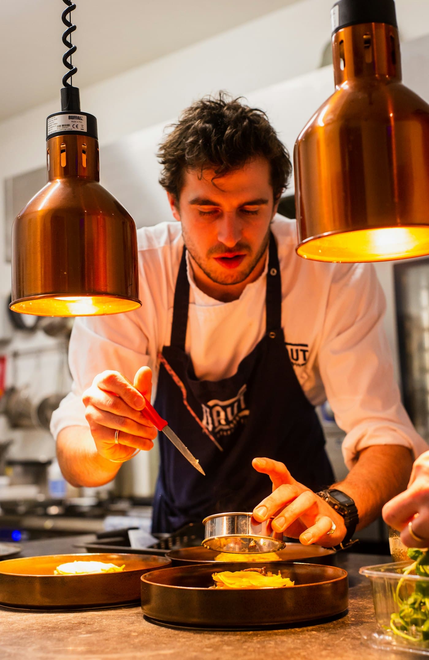 A chef plating under copper lamps